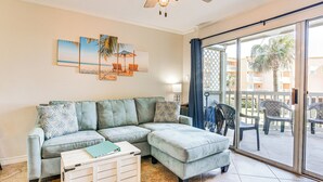 Una sala de estar con un sofá modular, una mesita y un ventanal corredero que da a un patio exterior con sillas.