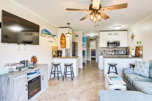 A modern kitchen with a central island, bar stools, a ceiling fan, and a TV mounted on the wall. - Galveston Vacation Rental - Walk to the Beach! (Galveston)