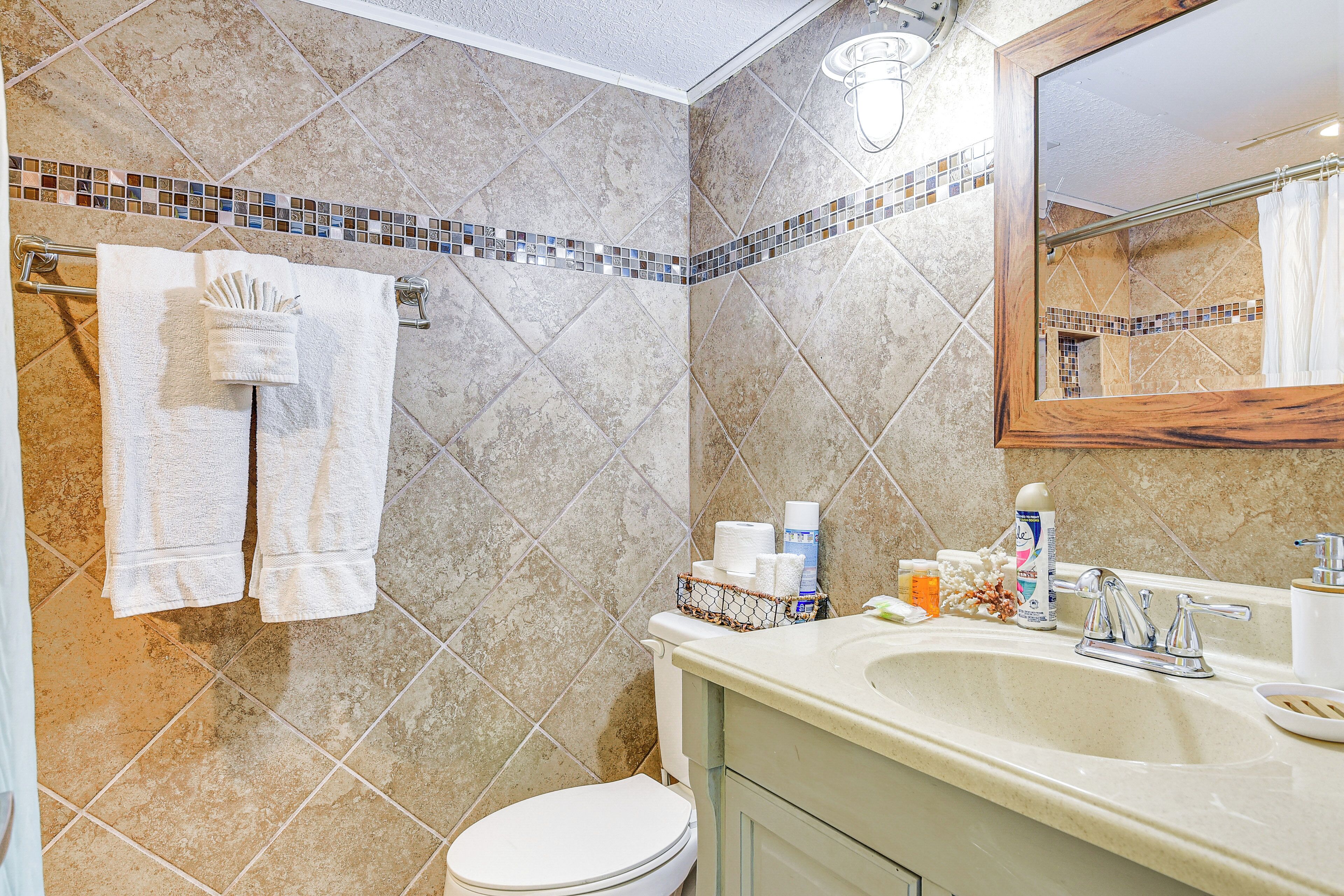A bathroom with a toilet, sink, and mirror. There are towels hanging on a rack, and toiletries on the sink counter.