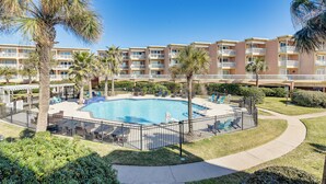 Un hotel con piscina central rodeada de palmeras y una valla.
