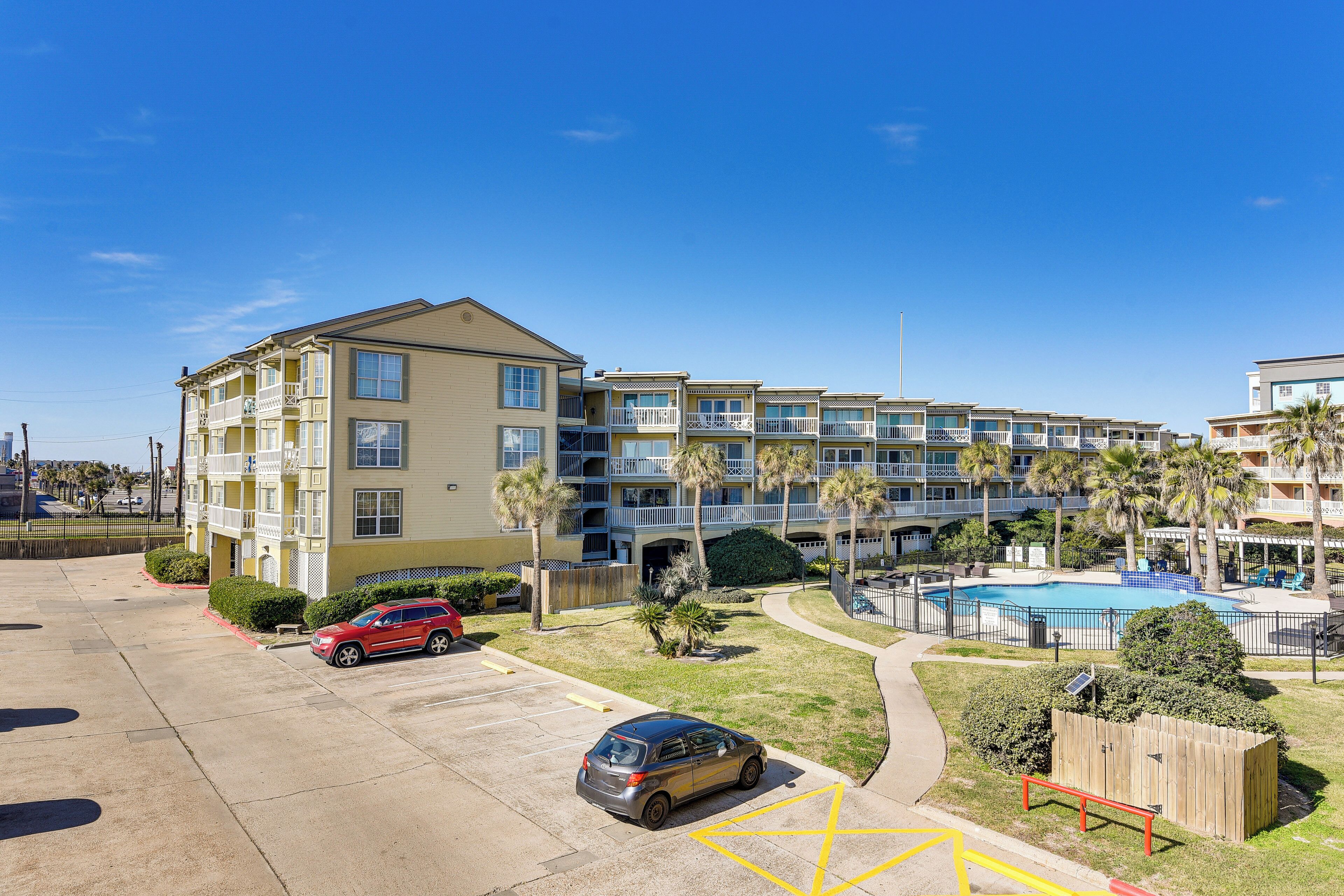 A multi-story hotel with balconies, a swimming pool, and a parking lot.