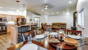 A spacious dining area with a wooden table set for four, surrounded by chairs. A kitchen with wooden cabinets and a built-in oven is visible in the background. - Family-friendly Fairbanks Home: Chena River Access (Fairbanks)
