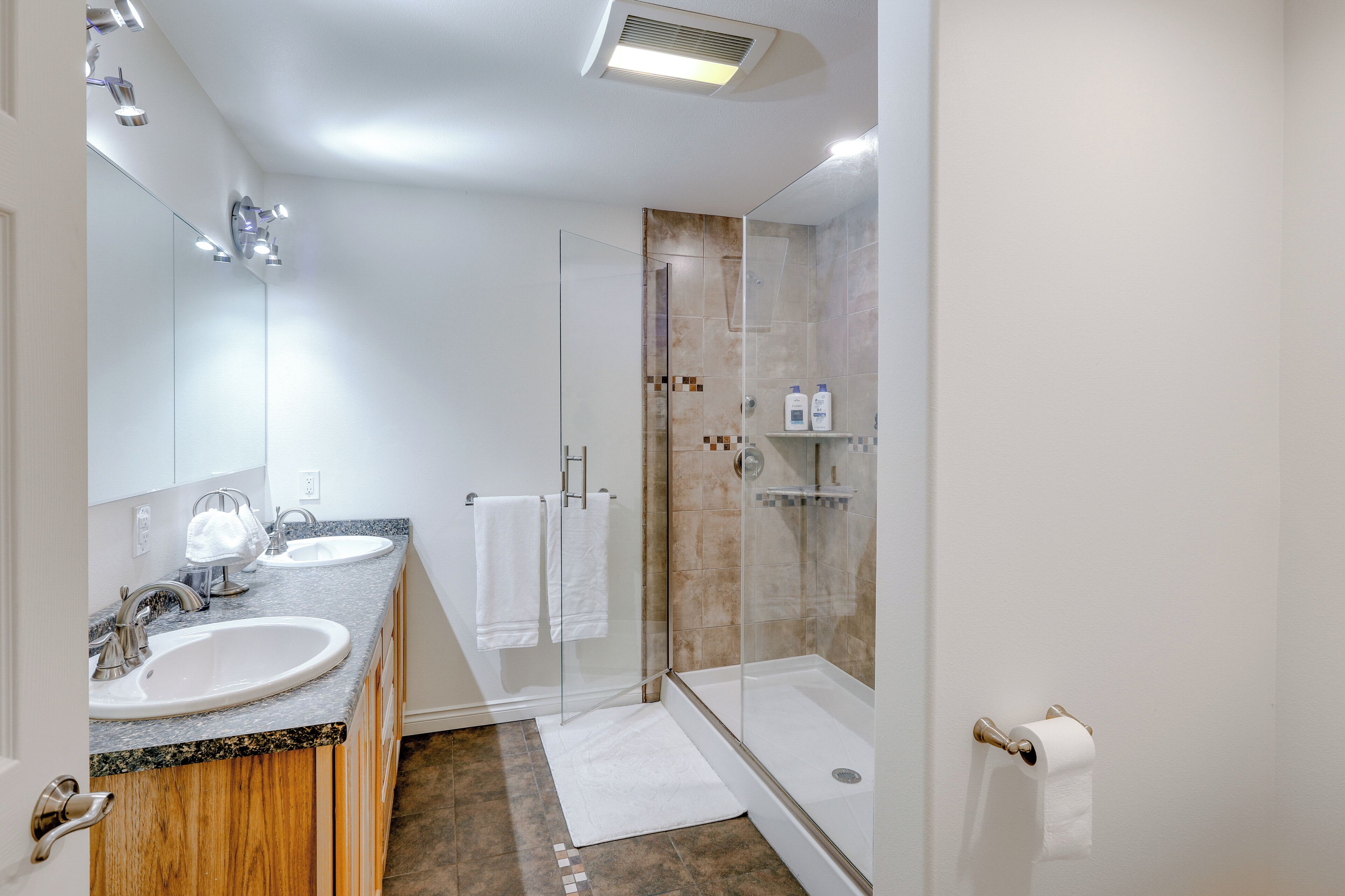 A modern bathroom with two sinks, a glass shower enclosure, and a white door.