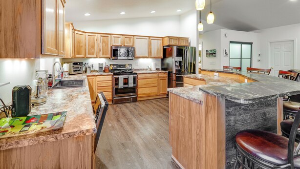 A modern kitchen with wooden cabinets, a central island, and bar stools. - Family-friendly Fairbanks Home: Chena River Access (Fairbanks)