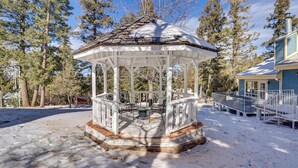 A gazebo with a wooden floor, surrounded by snow-covered ground and trees.