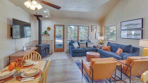 A spacious living area with a fireplace, a blue sofa, orange chairs, and a dining table set for four.