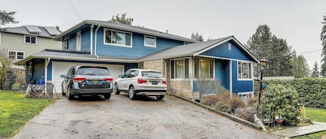 A two-story house with a garage, two cars parked in the driveway, and a well-maintained lawn.