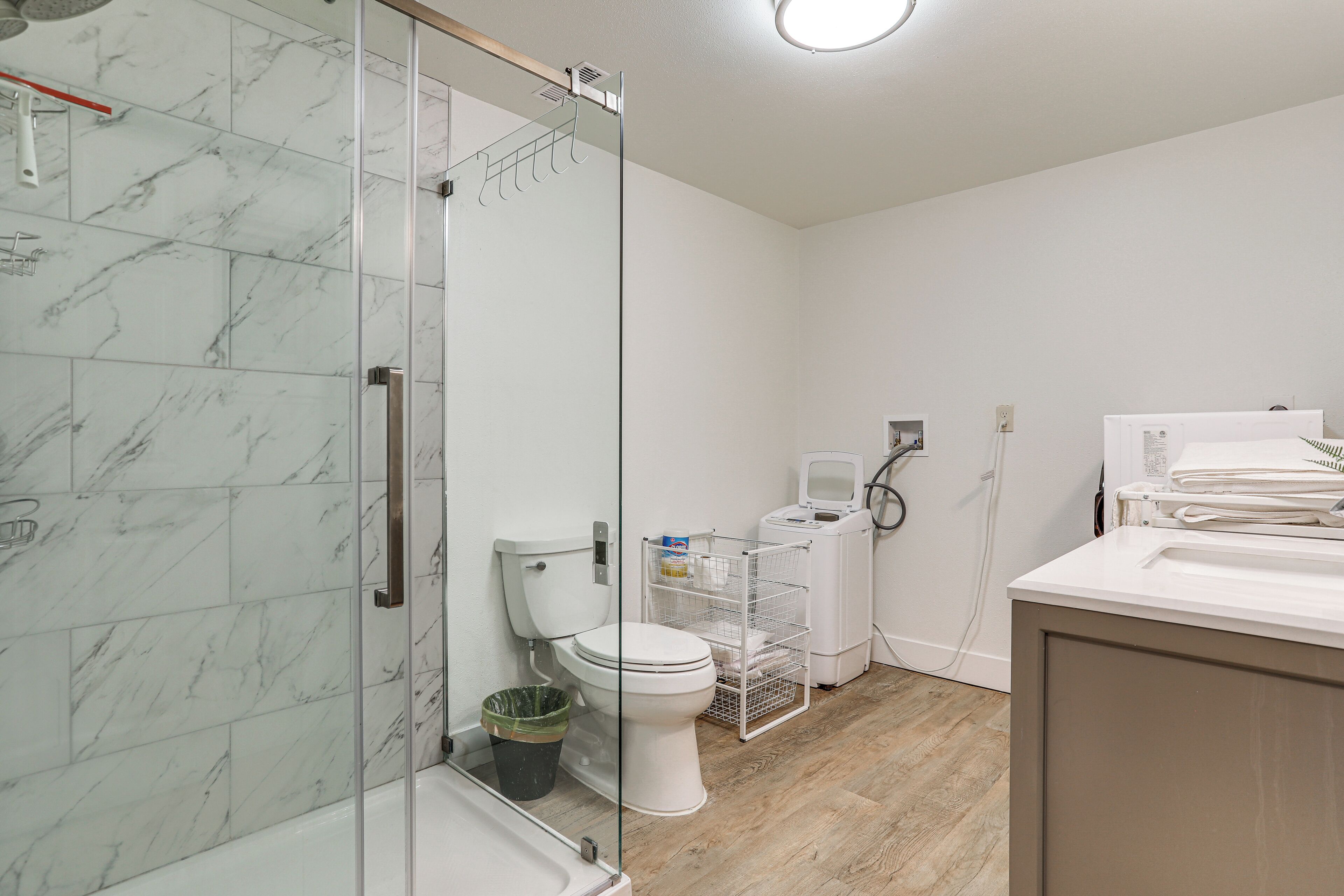 A bathroom with a glass shower enclosure, a toilet, a washing machine, and a sink.