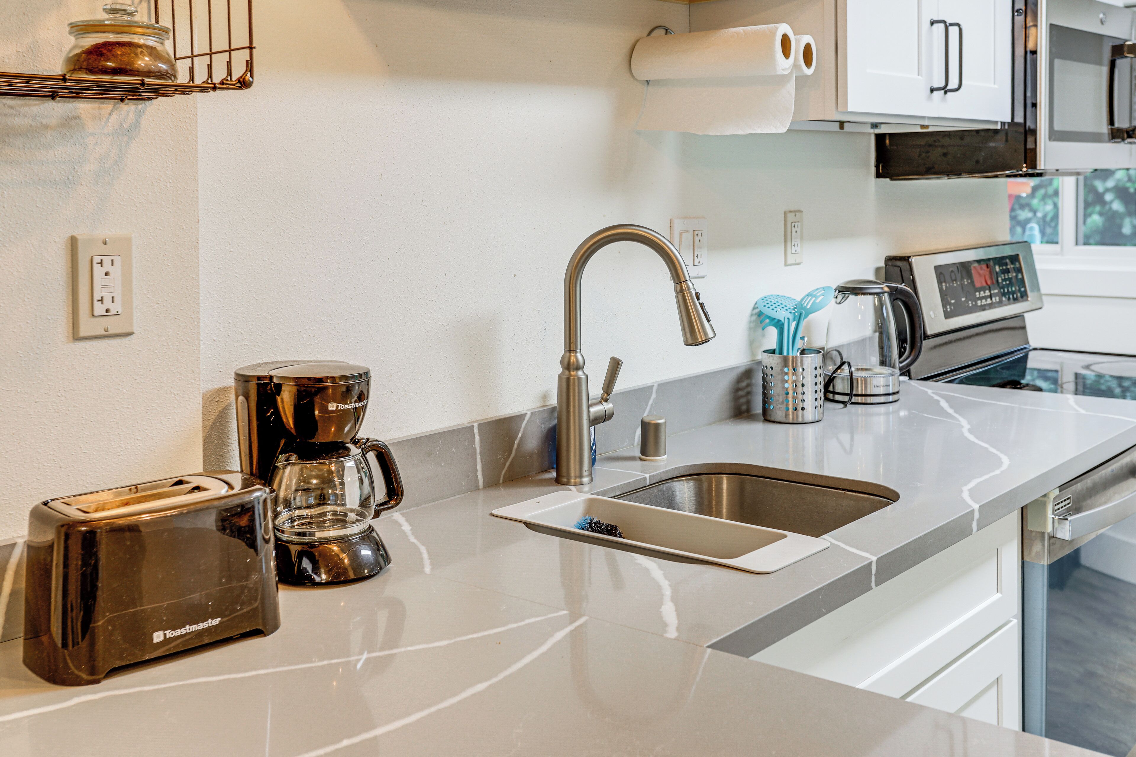 A modern kitchen with a stainless steel sink, a toaster, a coffee maker, and a microwave.