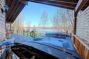 Ein Whirlpool mit einer Holzterrasse und Blick auf einen See und Bäume.