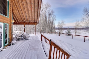 Una terraza de madera con mobiliario exterior y vistas a árboles y montañas nevadas.