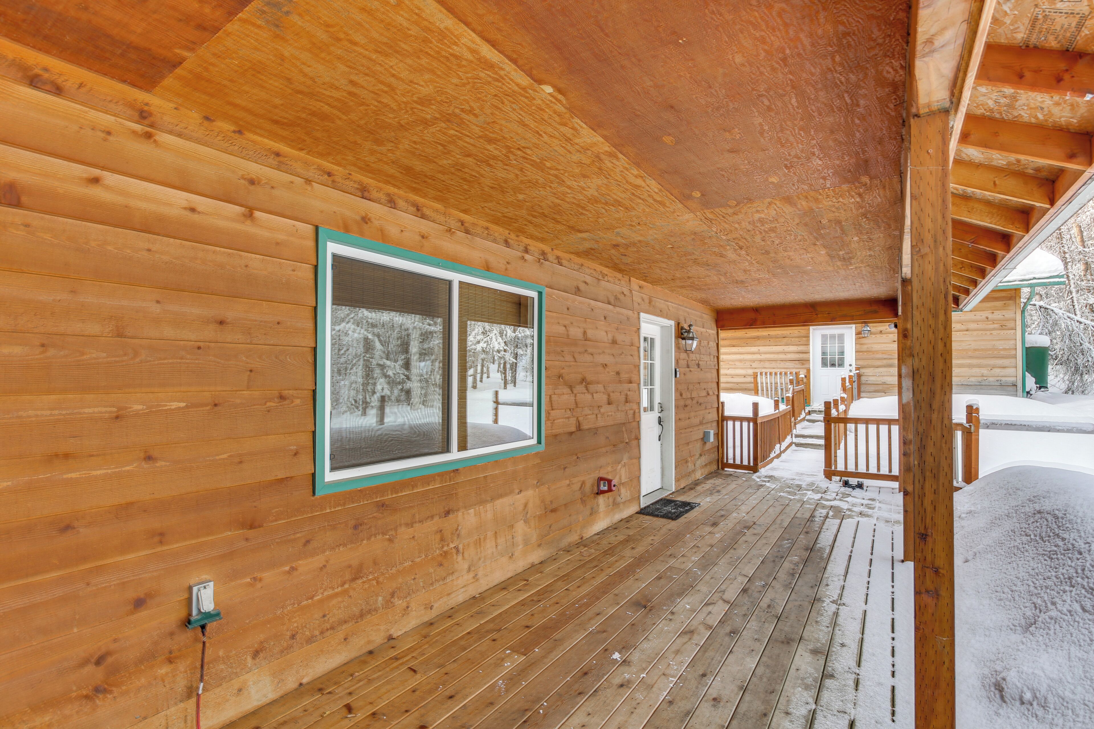 A wooden cabin with a covered porch, a window with a green frame, and a door.