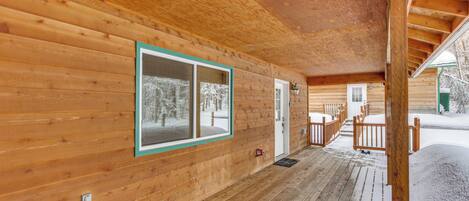 A wooden cabin with a covered porch, a window with a green frame, and a door.