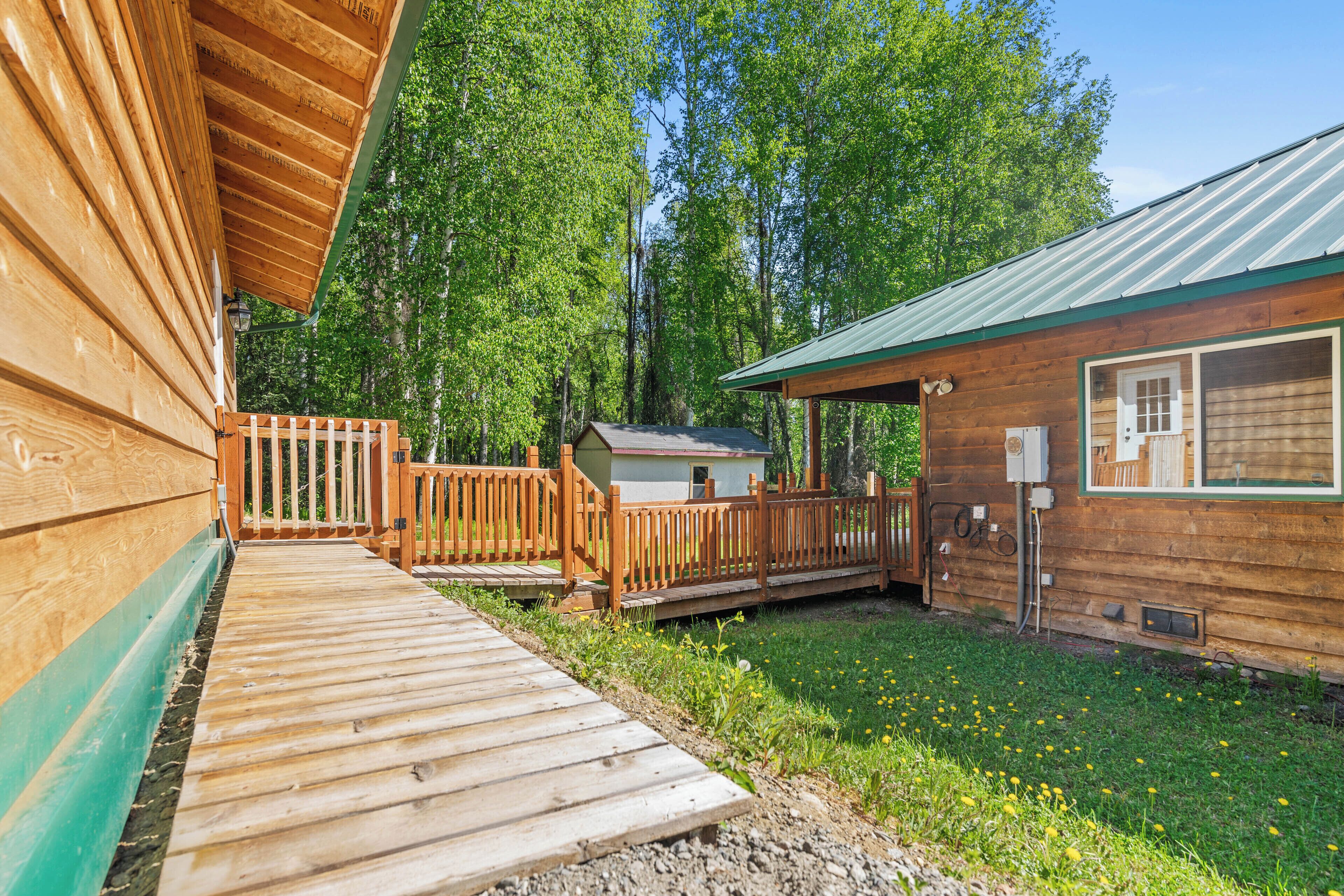 A wooden cabin with a deck, surrounded by a wooden fence and a grassy yard.