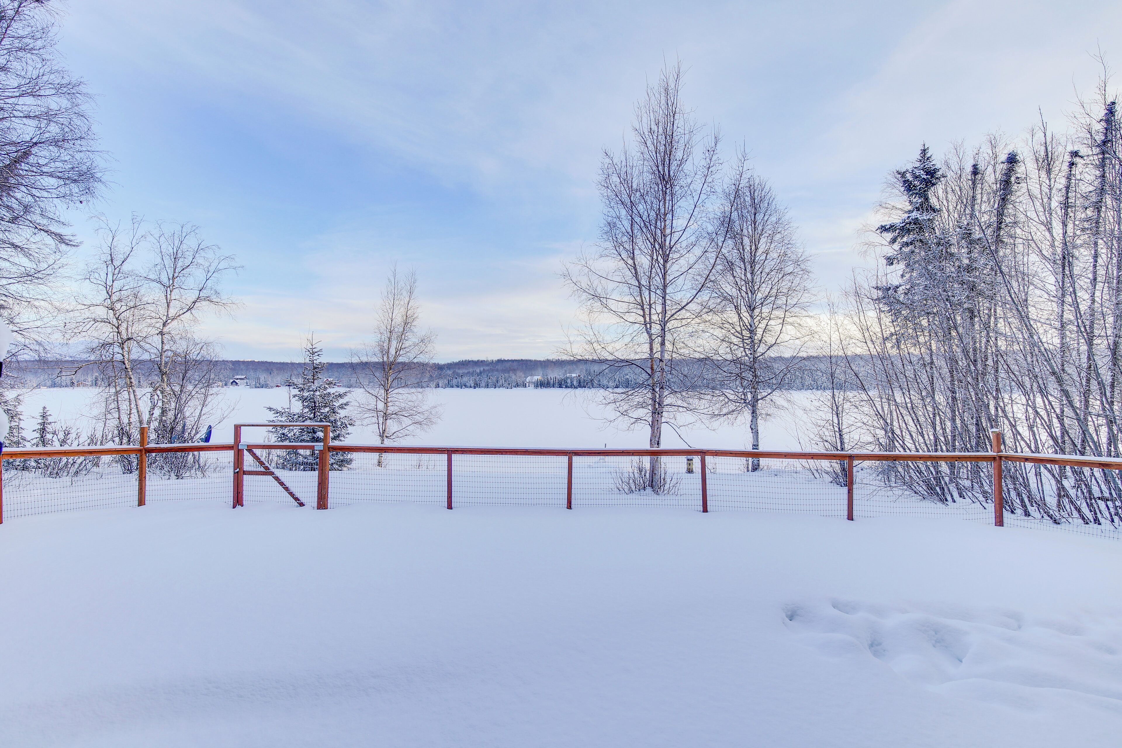 A snow-covered landscape with a wooden fence and trees.