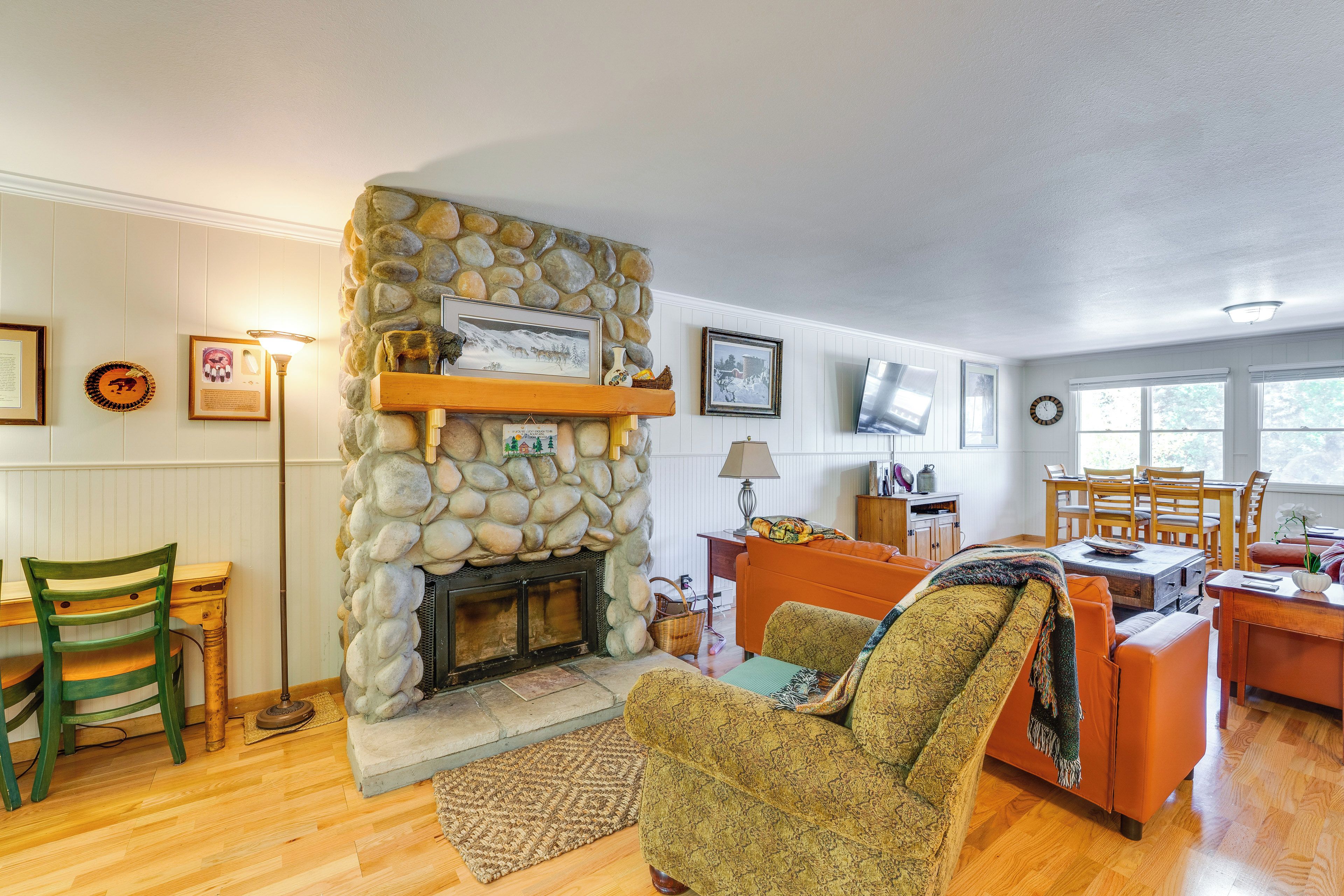 A cozy living room with a stone fireplace, wooden furniture, and various framed pictures on the walls.