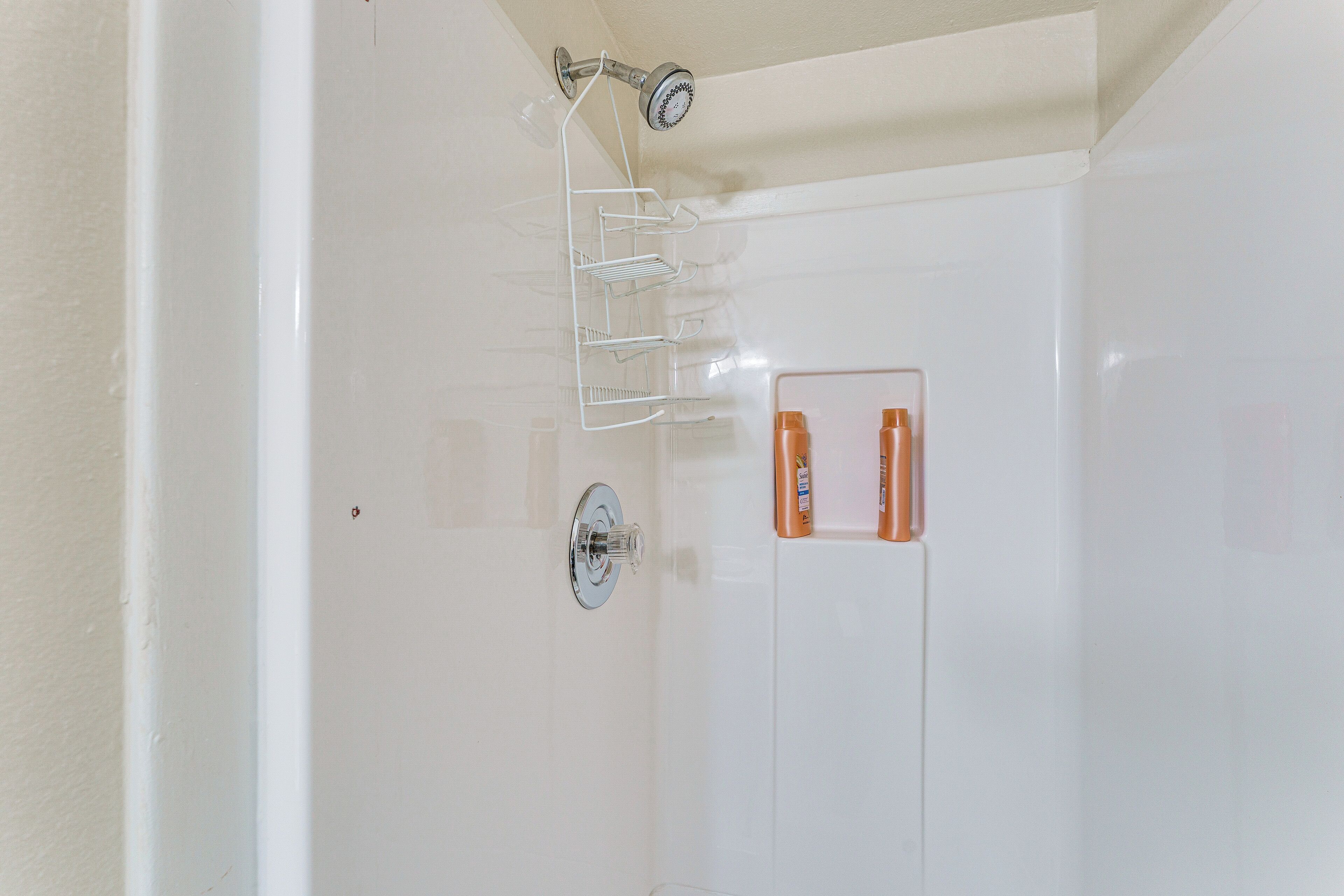 A bathroom with a shower, a glass shelf with toiletries, and a white tiled wall.