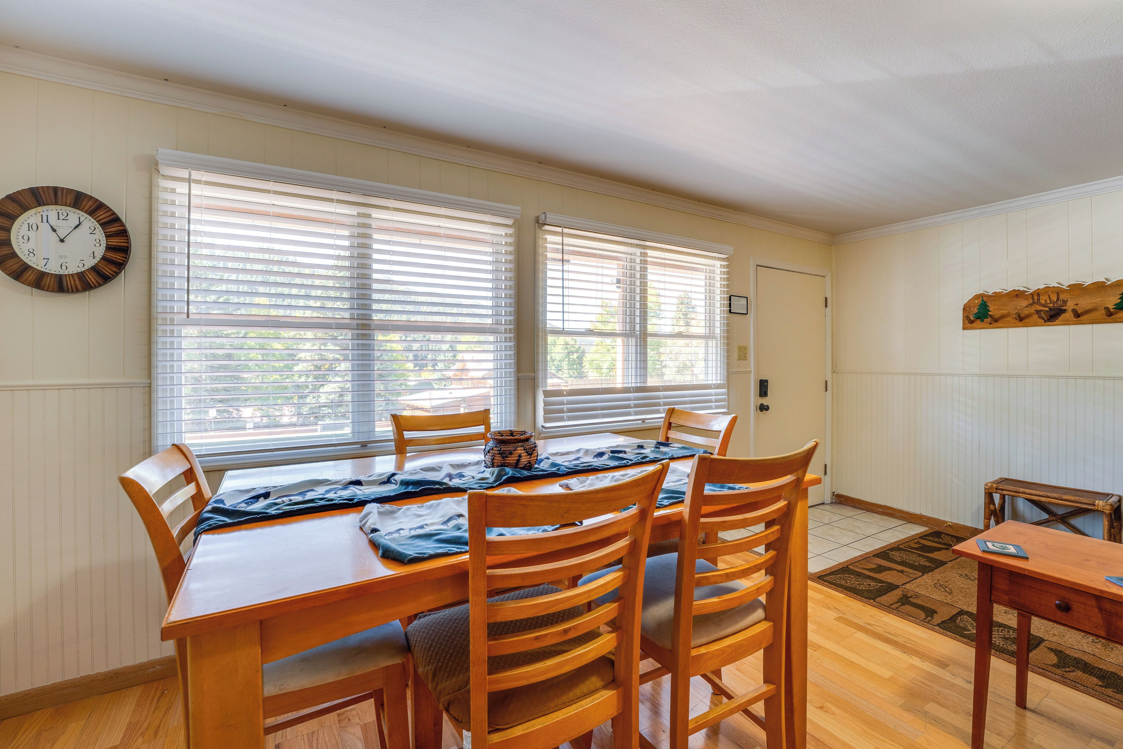 Comedor con mesa y sillas de madera, un reloj en la pared y un perchero junto a la puerta.
