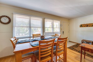 A dining room with a wooden table and chairs, a clock on the wall, and a door with a coat rack. - Main Street Red River Condo w/ Fireplace & Views! (Red River)