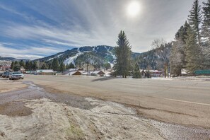 A wide, open road with a few cars parked on the side. There are buildings and trees in the background, and a mountain range is visible in the distance. - Main Street Red River Condo w/ Fireplace & Views! (Red River)