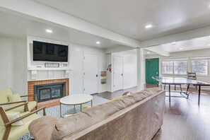 A living room with a fireplace, a flat-screen TV, a ping pong table, and a sofa. - Main Street Red River Condo w/ Fireplace & Views! (Red River)