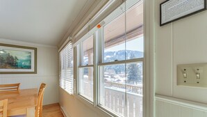 A dining area with a wooden table and chairs, large windows with blinds, a radiator, and a framed picture on the wall. - Main Street Red River Condo w/ Fireplace & Views! (Red River)