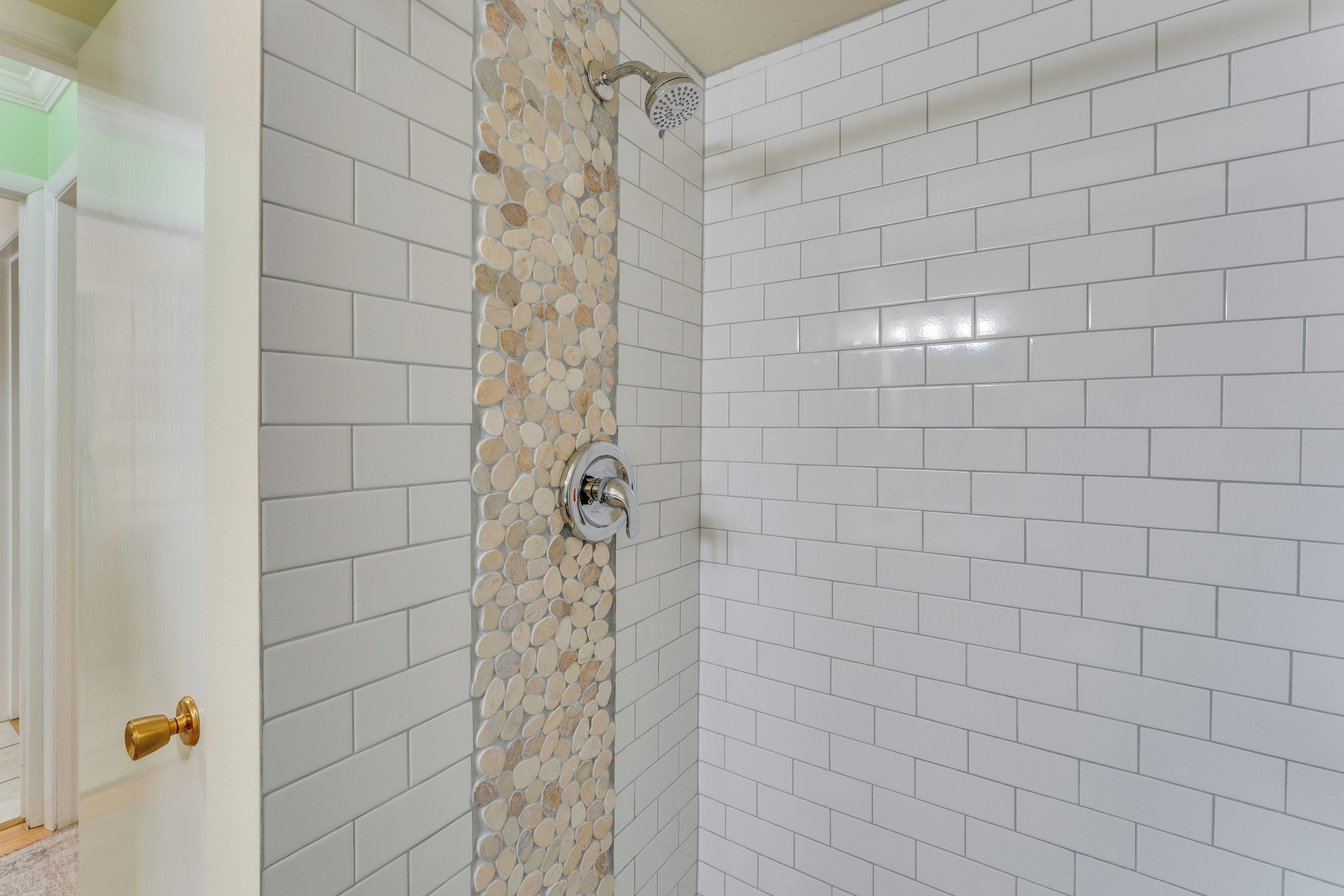 Een badkamer met witte betegeling, een douche met glazen deur en een gouden deurklink.