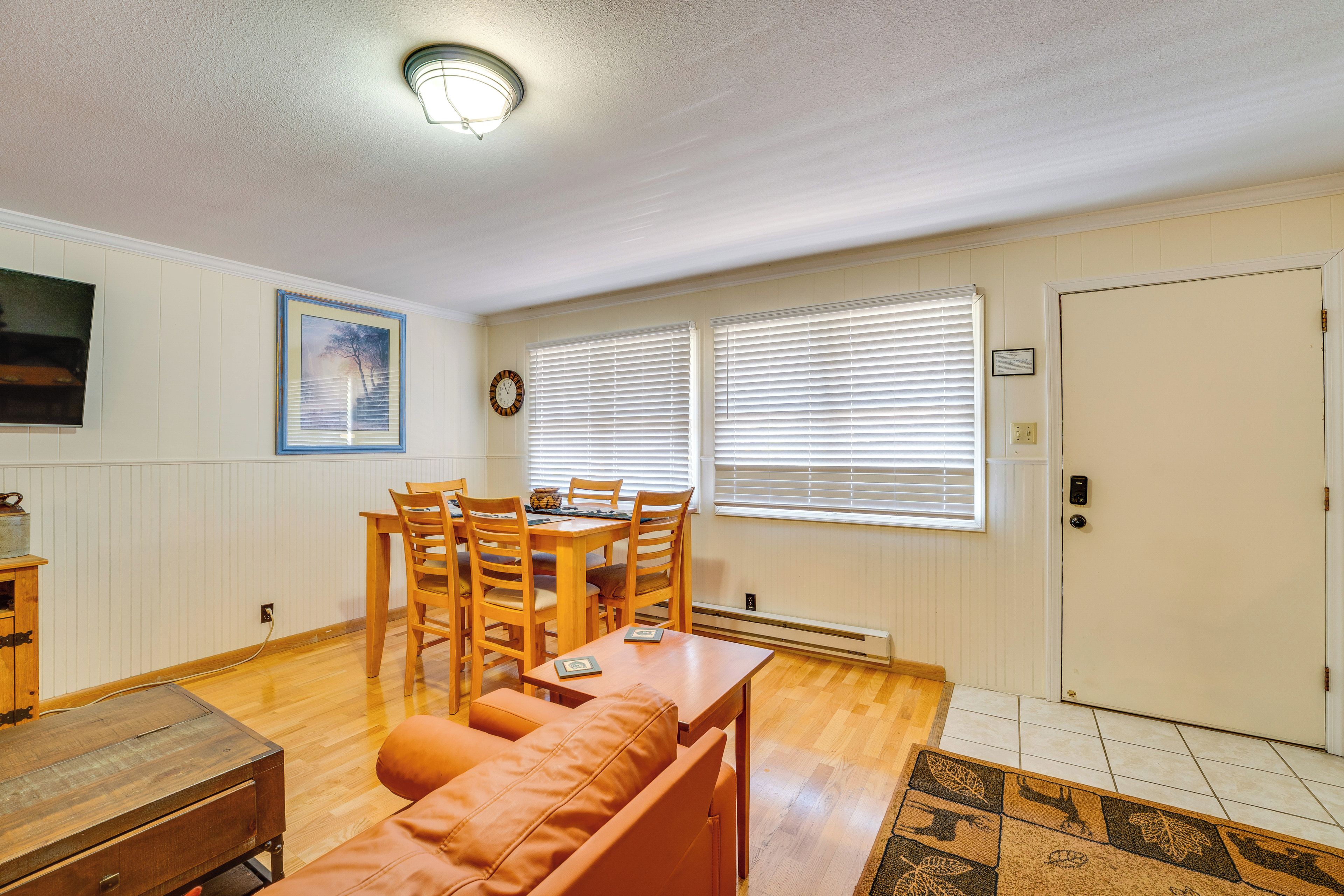 A dining area with a wooden table and chairs, a sofa, and a television on the wall.