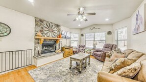 A living room with a fireplace, a ceiling fan, a sofa, and a coffee table. - Ruidoso Cabin Rental w/ Hot Tub: Near Midtown! (Ruidoso)