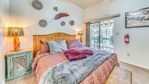A bedroom with a wooden headboard, patterned bedding, decorative wall art, and a view through a glass door. - Ruidoso Cabin Rental w/ Hot Tub: Near Midtown! (Ruidoso)