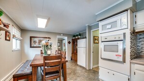 A spacious kitchen with a stone floor, wooden dining table, and white cabinetry. - Rector Home w/ Hot Tub ~ 6 Mi to Ligonier! (Ligonier)