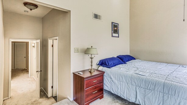 A bedroom with a bed, a nightstand, a lamp, and a door leading to another room.