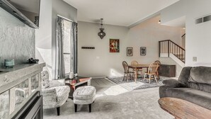 A modern living room with a fireplace, a dining area, and a staircase leading to an upper level.