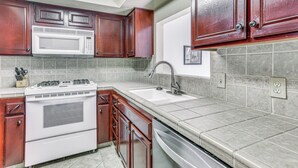 A kitchen with wooden cabinets, a white stove, a microwave, and a sink.