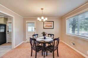 A dining area with a round table, dark chairs, a chandelier, a potted plant, and a window with blinds. - Greenville Home w/ Private Yard Near Downtown! (Greenville)