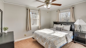 A bedroom with a bed, a nightstand, a ceiling fan, and a window with curtains.