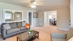 A living room with a sofa, coffee table, and a ceiling fan. There is a dining area with a table and chairs in the background.