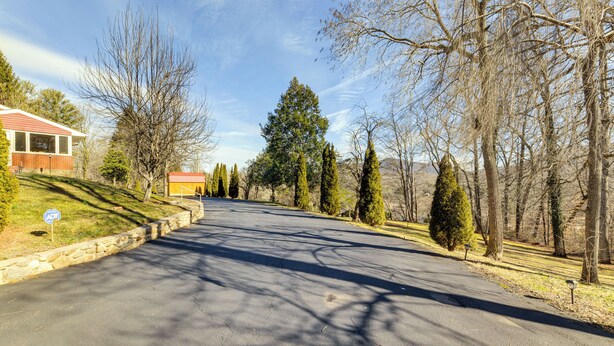 A residential street with a house on the left, a stone wall, and a row of trees. - Waynesville Studio Suite < 1 Mi to Downtown! (Waynesville)