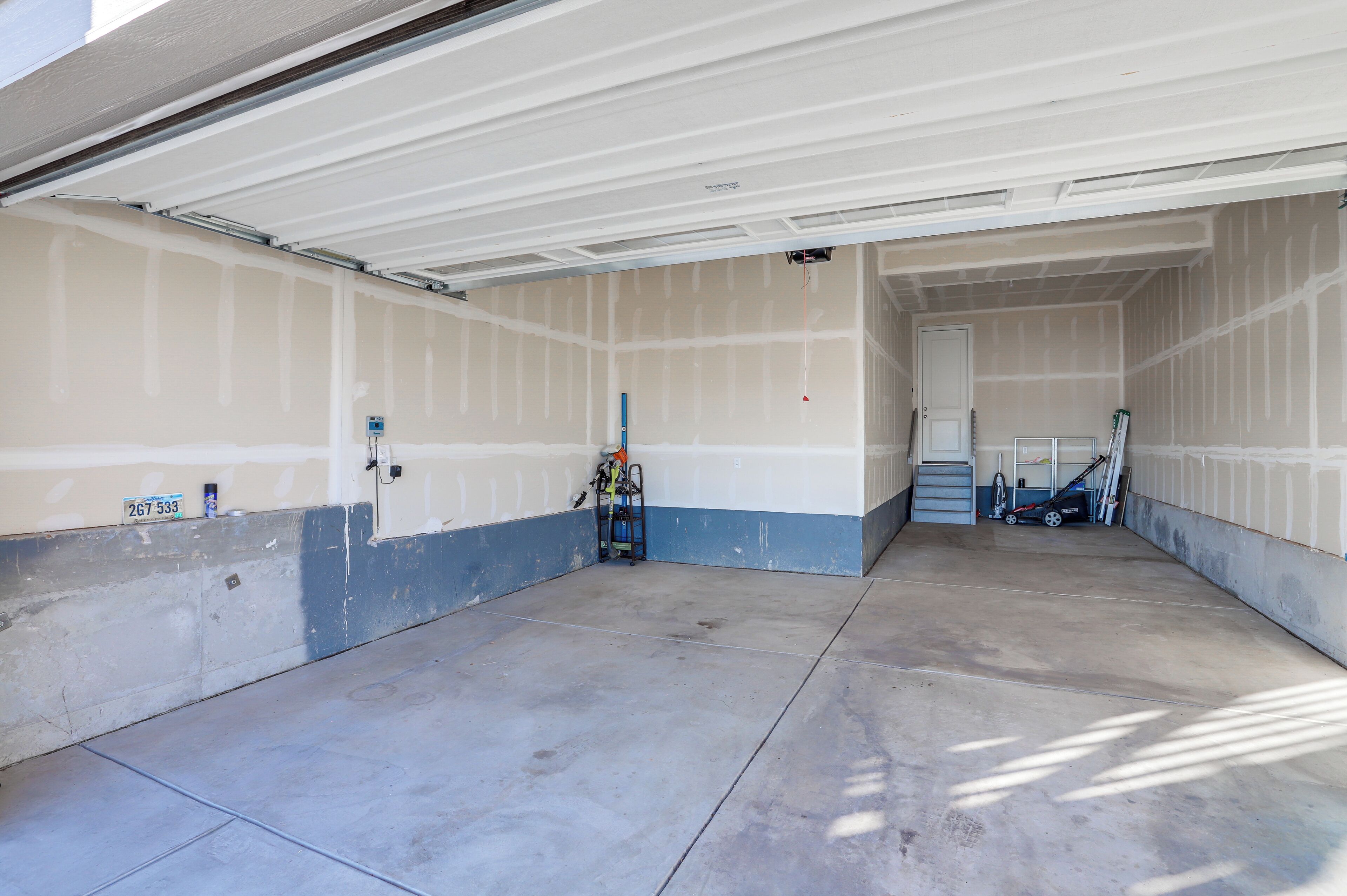 En garage med beton gulv, dør til en trappe og en væg i blå og hvid.