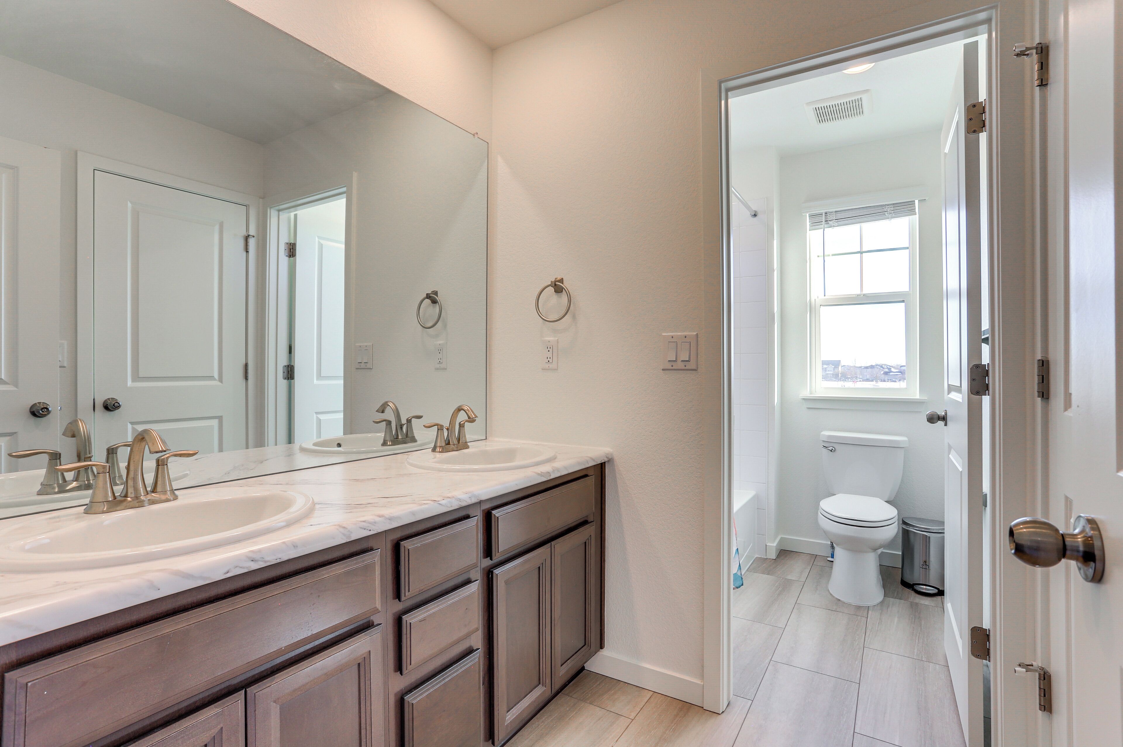 A bathroom with a double sink vanity, a toilet, and a window.