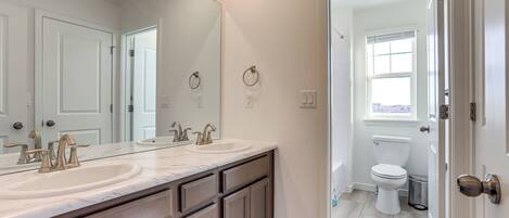 A bathroom with a double sink vanity, a toilet, and a window.