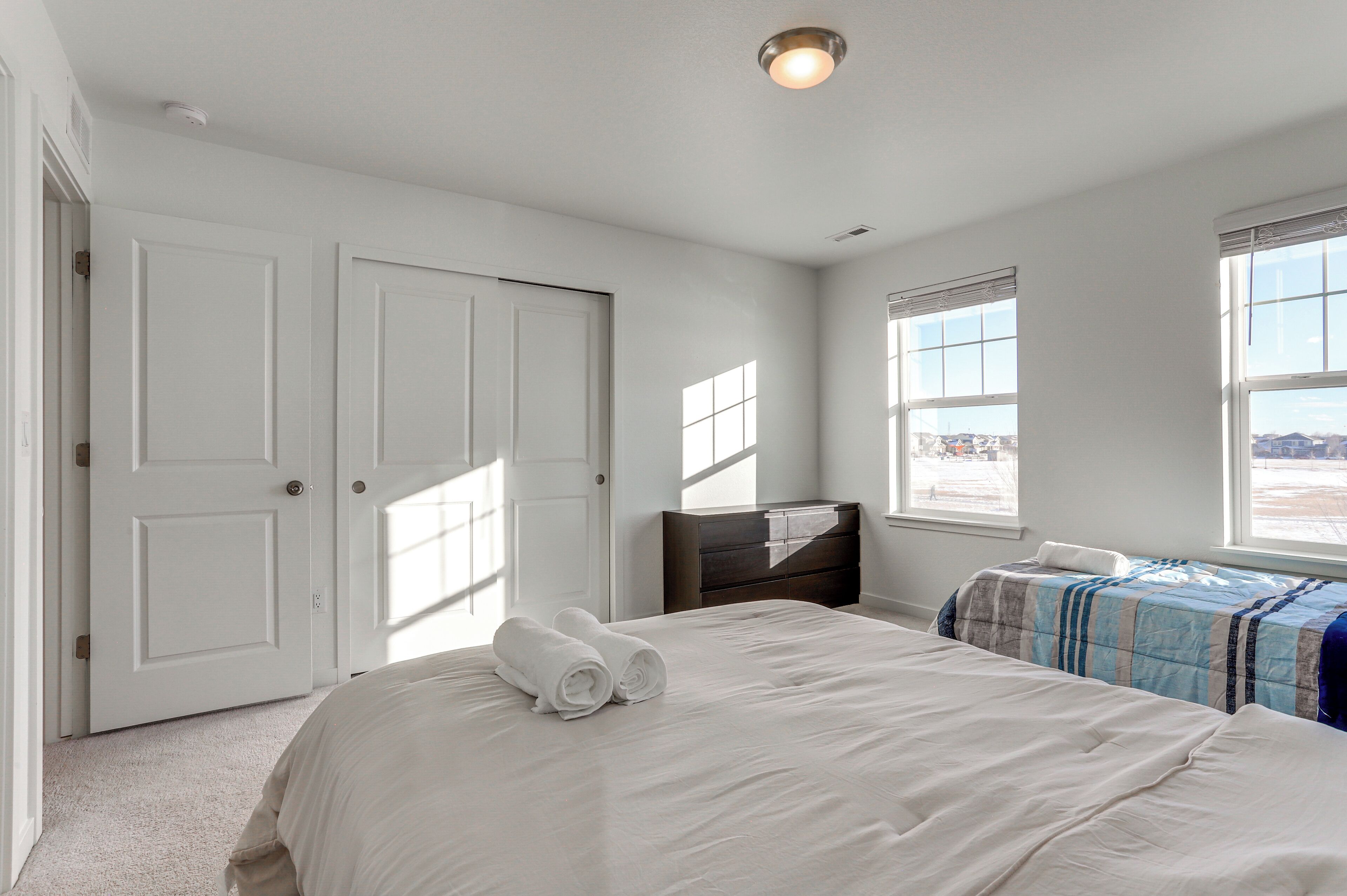 A bedroom with two beds, a dresser, and two windows.