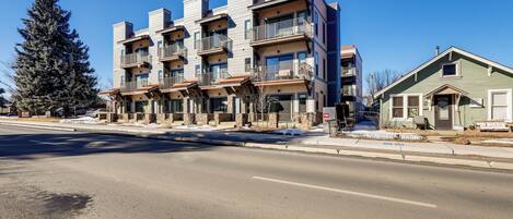A multi-story residential building with balconies, a driveway, and a snow-covered ground.