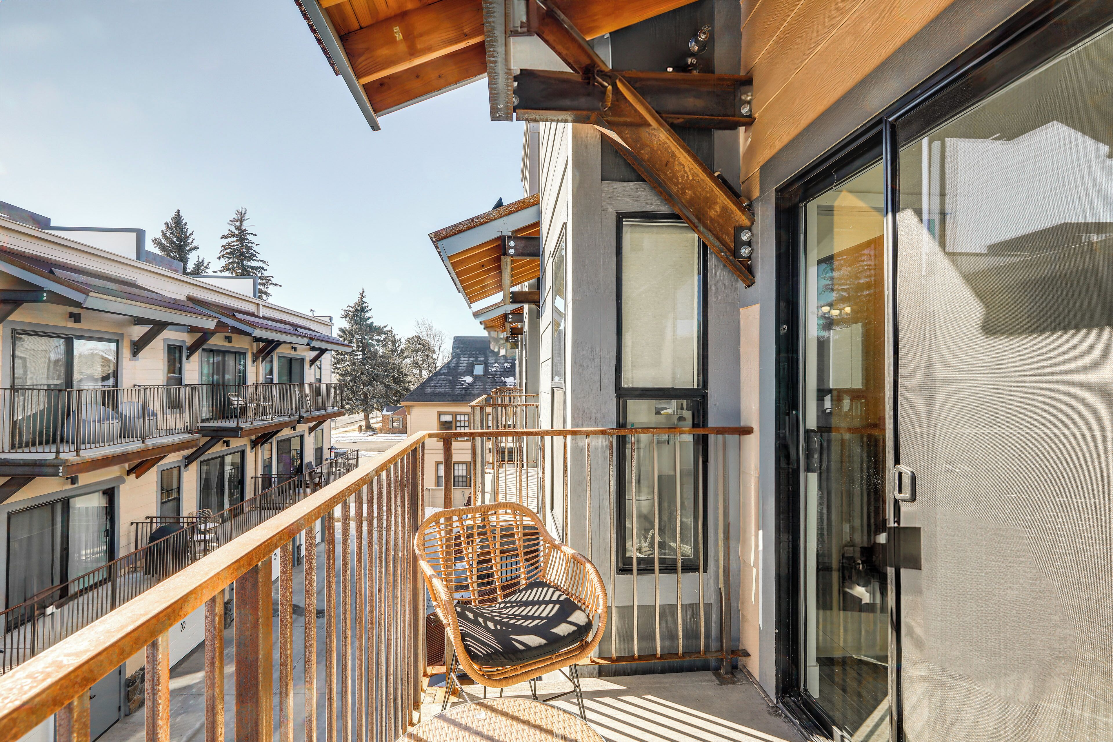 A balcony with a wicker chair and a glass door leading to a room.