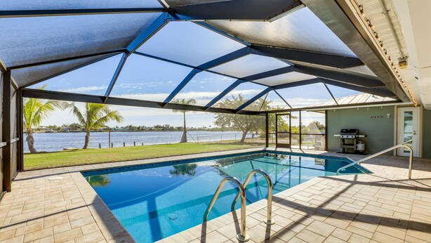 Piscina interna com vista para a água e palmeiras, rodeada por um espaço de área coberta.