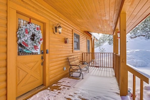 Une cabane en bois avec un porche, une terrasse recouverte de neige et une couronne accrochée à la porte.