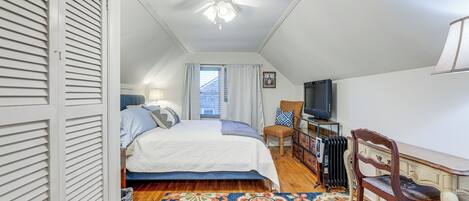 A bedroom with a bed, a desk, a chair, a television, and a ceiling fan.