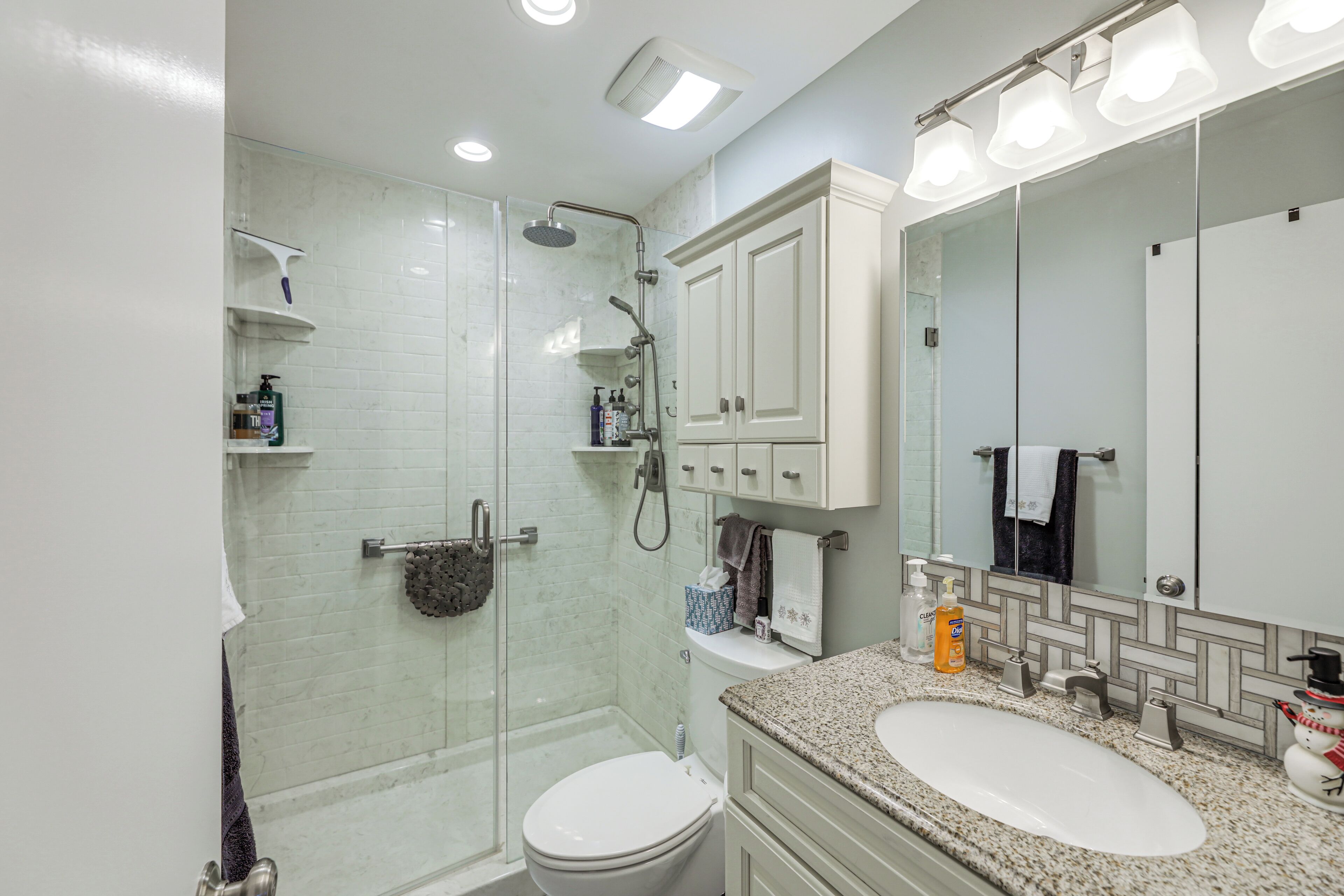 A modern bathroom with a glass-enclosed shower, a white toilet, a sink with a granite countertop, and a large mirror.