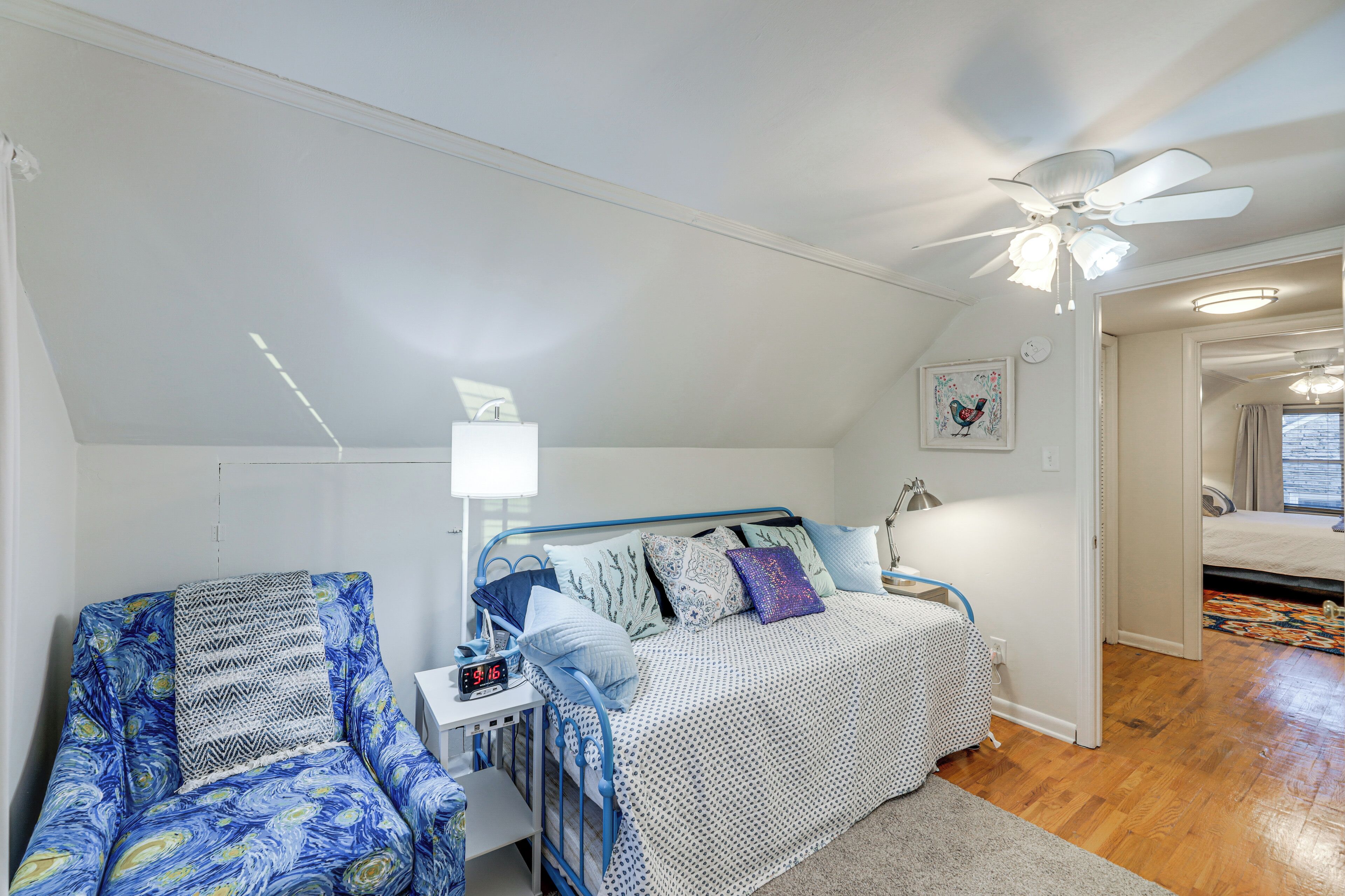 Ein Schlafzimmer mit einem Bett, einem Sessel, einem Nachttisch, einem Deckenventilator und einer Tür zu einem anderen Raum.