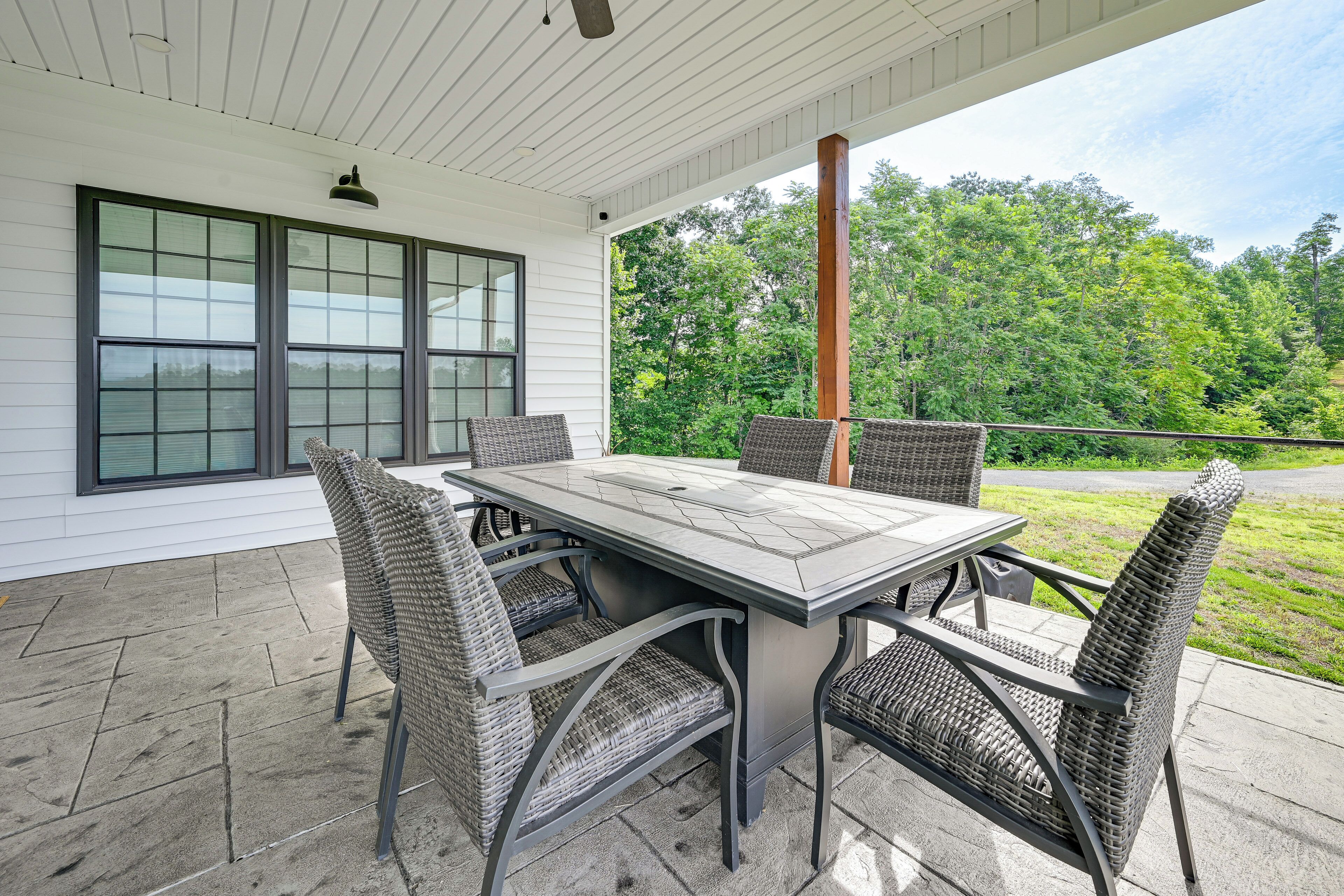 A covered patio with a table and chairs, a window, and a view of greenery.